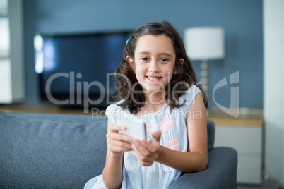 Happy girl sitting on sofa and using mobile phone in living room