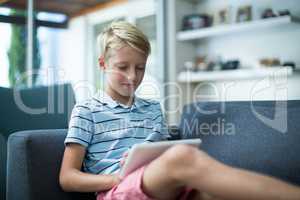 Boy sitting on sofa and using digital tablet in living room