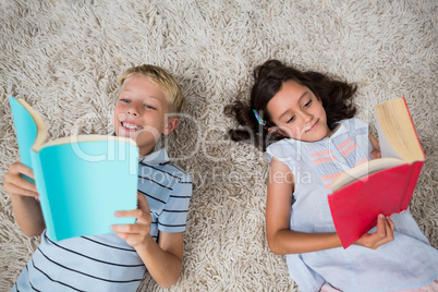 Siblings lying on rug and reading book in living room