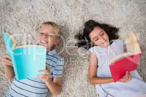 Siblings lying on rug and reading book in living room
