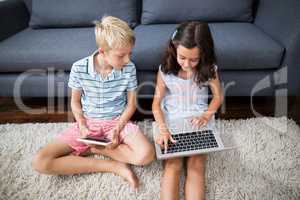 Siblings using digital tablet and laptop in living room