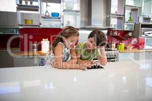 Happy siblings using digital tablet in kitchen