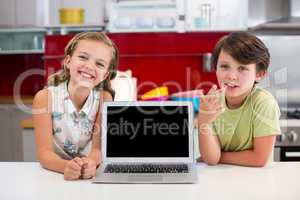 Smiling siblings with laptop on worktop in kitchen