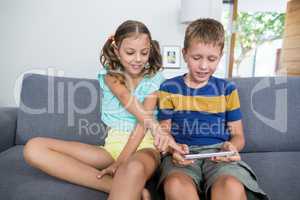 Smiling siblings using digital tablet on sofa in living room