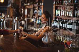 Female bar tender giving glass of beer to customer