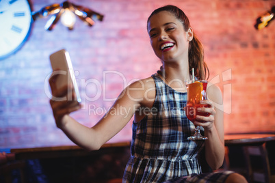 Young woman using mobile phone while having cocktail drink