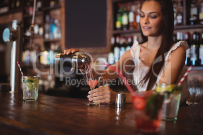 Female bartender pouring cocktail drink in the glass