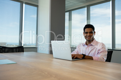 Portrait of smiling businessman using laptop in conference room