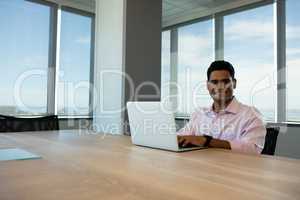 Portrait of smiling businessman using laptop in conference room
