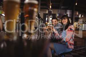 Portrait of happy couple holding glasses of beer at counter