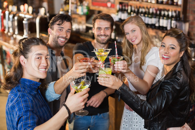 Portrait of happy friends holding drinks while standing in bar