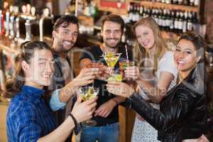 Portrait of happy friends holding drinks while standing in bar