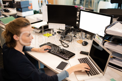 Businesswoman typing on laptop while using desktop pc