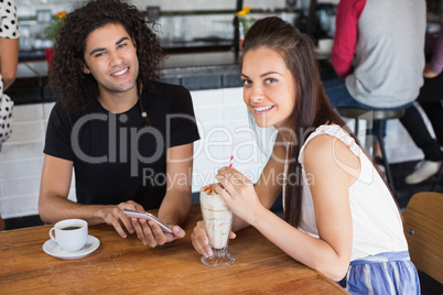 Portrait of smiling couple using mobile phone while having drinks in restaurant