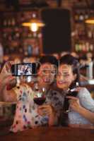 Young women taking a selfie from mobile phone while having a red wine