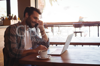 Man talking on mobile phone while using laptop