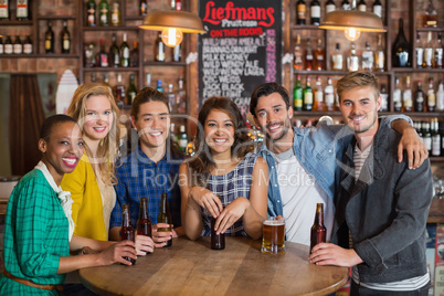 Portrait of young friends with beers by table in pub