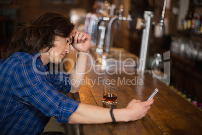 Depressed young man using mobile at pub