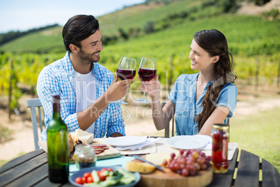 Smiling couple toasting red wine glasses while sitting at table