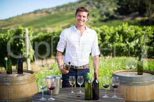 Portrait of young man holding wine bottle by table at vineyard