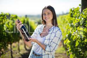 Portrait of young woman holding wine bottle at vineyard