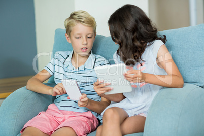 Siblings using digital tablet and mobile phone in living room