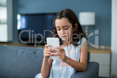Unhappy girl sitting on sofa and using mobile phone in living room