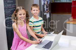 Siblings using digital tablet and mobile phone in kitchen