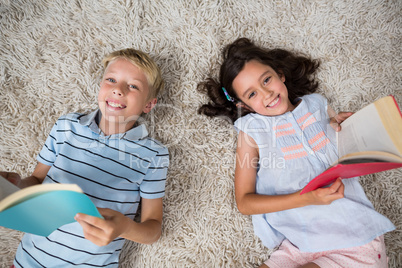 Portrait of siblings lying on rug and reading book in living room