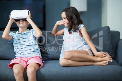 Girl looking at her brother using virtual reality headset in living room
