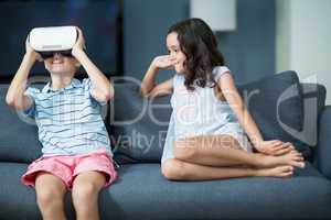 Girl looking at her brother using virtual reality headset in living room