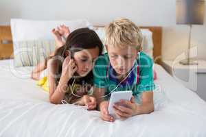 Siblings listening to music while using mobile phone on bed