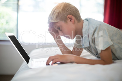 Tense boy using laptop on bed in bedroom