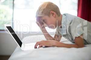 Tense boy using laptop on bed in bedroom