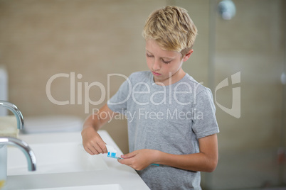 Boy putting toothpaste on brush in bathroom