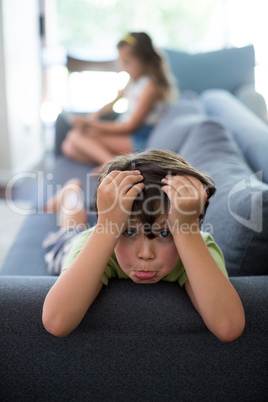Upset boy lying on sofa while girl using digital tablet in living room
