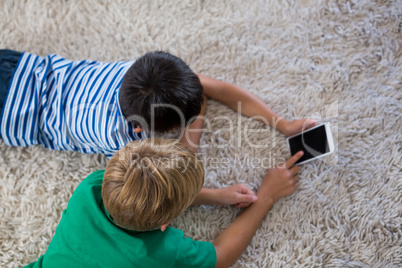 Siblings lying on rug and using mobile phone in living room