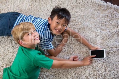 Portrait of happy siblings lying on rug and using mobile phone