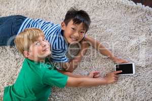 Portrait of happy siblings lying on rug and using mobile phone