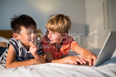 Smiling siblings using laptop on bed