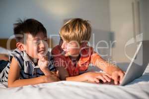 Smiling siblings using laptop on bed