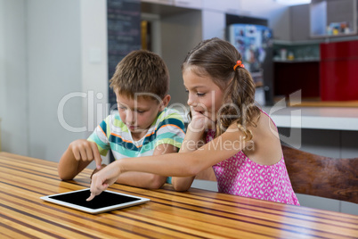 Siblings using digital tablet in kitchen