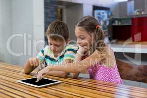 Siblings using digital tablet in kitchen