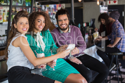 Cheerful friends discussing over mobile while having drink in restaurant