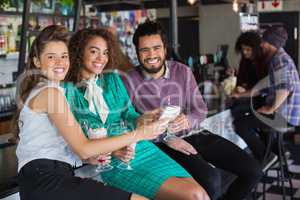 Cheerful friends discussing over mobile while having drink in restaurant