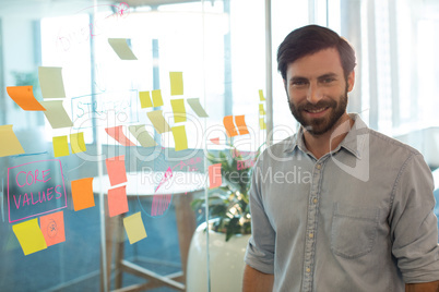 Portrait of confident businessman standing by strategy on glass at office