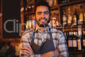 Portrait of smiling waiter standing with arms crossed