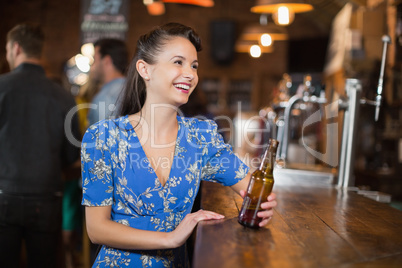 Happy woman looking away while holding beer bottle