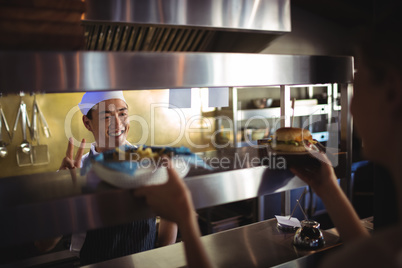 Chef passing tray with french fries and burger to waitress