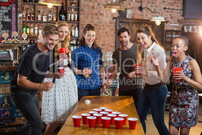 Friends cheering while man playing beer pong in bar